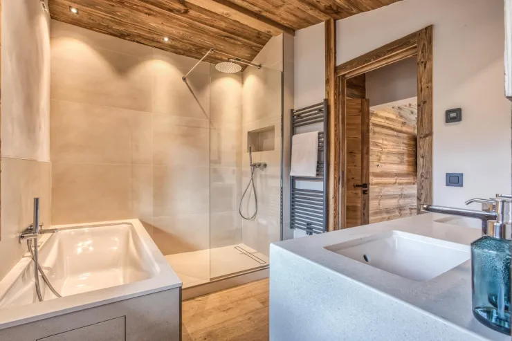 The bathroom for the master bedroom with its bath and sink in burgundy stone. It has a wooden floor and ceiling and soft ligting. 