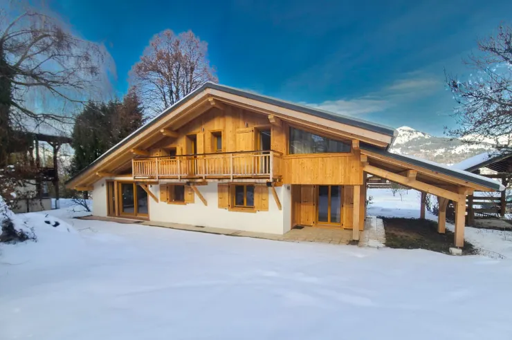 Exterior view of the chalet under the snow, with the mountains in the background