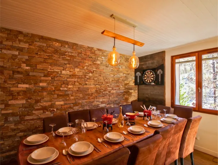 The table is carefully set for a group meal accommodating up to 14 people. Fondue sets are placed in the center, illustrating the warm and convivial experience of a winter sports holiday with family or friends.